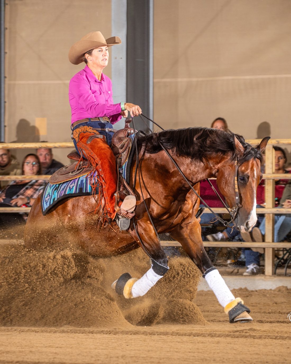 Iris Austin riding a bay reining horse through a sliding stop